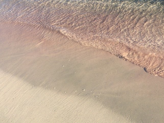 The shore of Elafonissi beach with pink colored coral mixed in with the sand. 